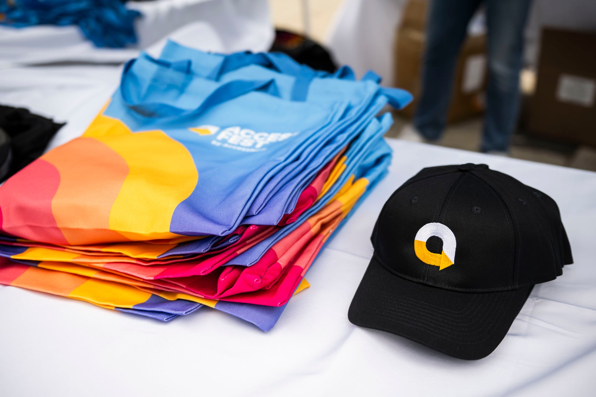 Colorful tote bags and a black cap with logo on a white table cloth