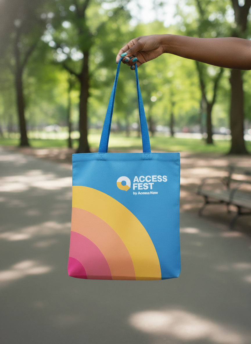 Blue tote bag with colorful design and 'Access Fest' logo held in a park.